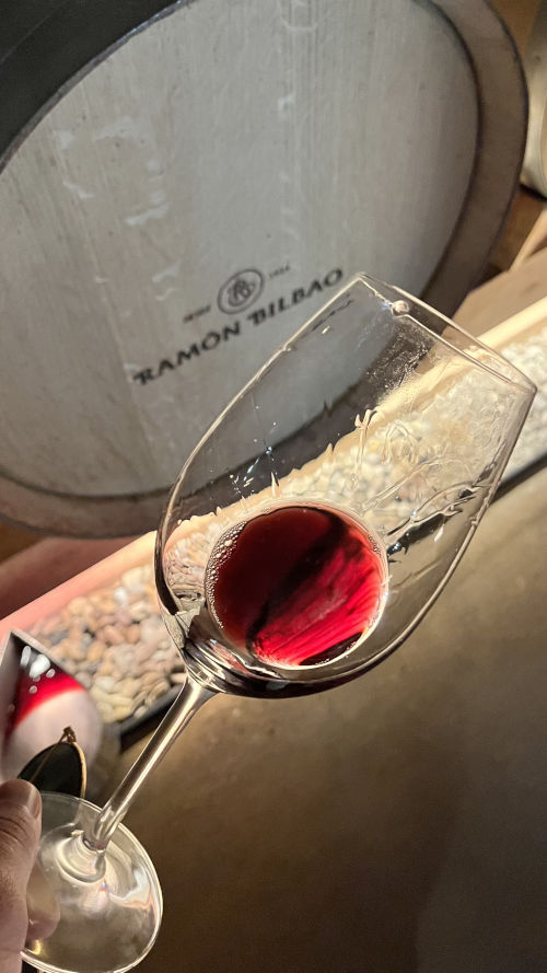 A glass of red in front of a Ramon Bilbao barrel